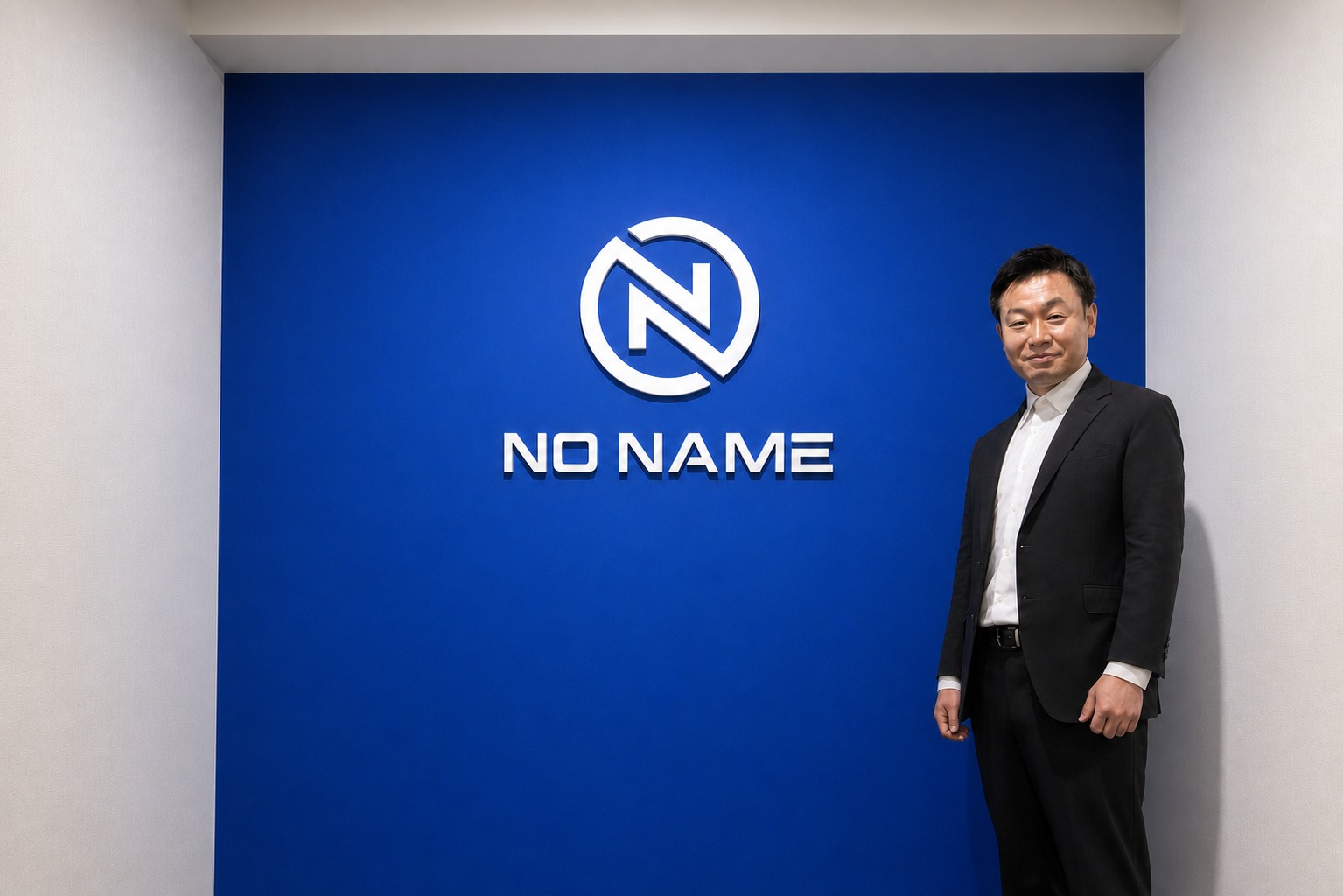 NO NAMEロゴ前に立つ安間信裕氏の横長写真